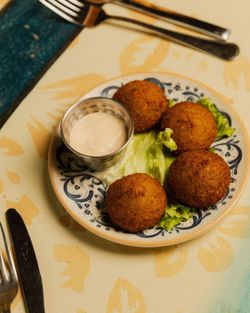 Polpette croccanti servite su un piatto con foglie di lattuga e salsa a parte, ambiente di ristorante