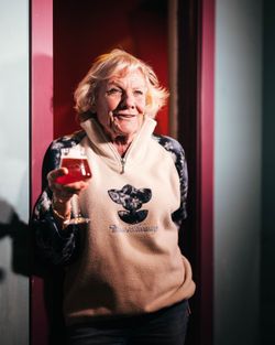 Donna con giacca chiara tiene in mano un bicchiere di birra artigianale davanti a una porta di colore rosso scuro.