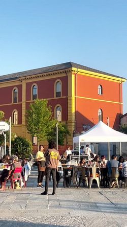 Open Baladin Roma mit Gästen im Außenbereich, mehreren Tischen und einem weißen Zelt bei sonnigem Wetter.