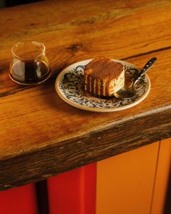 Tiramisu sur une assiette décorative avec une cuillère, accompagné d'un verre de café sur une table en bois rustique.