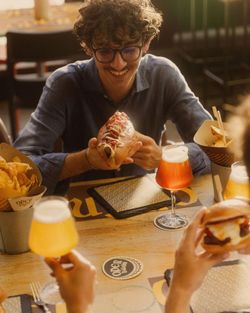 Uomo sorride mentre tiene un hot dog accompagnato da birra artigianale in un ambiente accogliente.