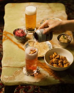 Birra artigianale versata in un bicchiere su un tavolo con ciotole di cibo e una birra Baladin sullo sfondo.