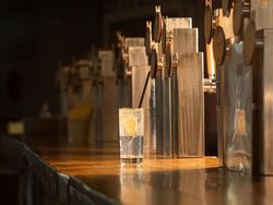 Bar du restaurant Open Baladin Torino avec une rangée de tireuses à bière et un verre d'eau avec une tranche de citron.