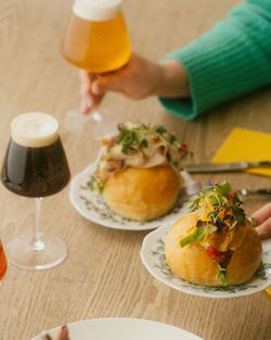 Two gourmet hamburgers on plates with fresh greens, paired with glasses of craft beer on a wooden table.