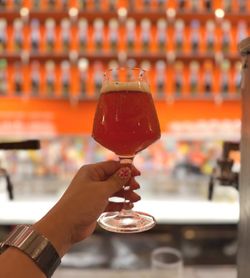 Verre de bière artisanale Baladin tenu à la main devant un comptoir avec robinet à bière et fond orange flou.
