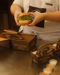 Hamburger con insalata preparato da un cuoco, accanto ci sono scatole da asporto personalizzate Open Baladin.