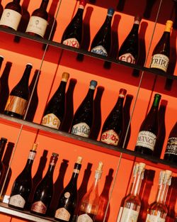 Bouteilles de birra artigianale alignées sur des étagères contre un mur orange dans Open Baladin Torino.