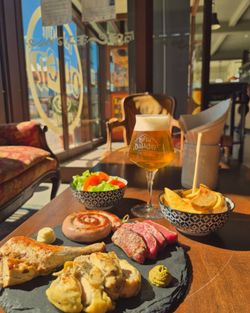Craft beer and plates with meat and sides, including salad and bread, on a table at Open Baladin Roma.