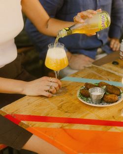 Birra artigianale Baladin versata in calice al tavolo di legno con contorno di crocchette e salsa bianca.