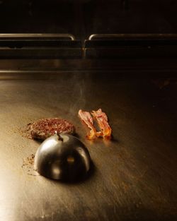Auf einer Grillplatte braten Hamburger-Patty und zwei Streifen Speck nebeneinander, dampfend und frisch zubereitet.
