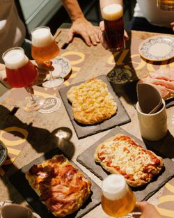 Diverse Craft-Biere in Gläsern und verschiedene flache Pizzen auf schwarzen Steinplatten auf dem Tisch serviert.
