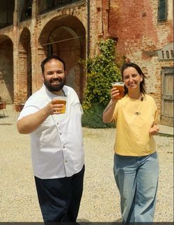 Zwei Personen stehen draußen vor einem historischen Backsteingebäude und halten Biergläser hoch.
