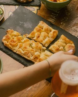 Flatbread with a golden crust served on a slate plate, alongside a glass of craft beer in hand.