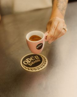 Tazzina rosa con caffè espresso tenuta da una mano sopra un sottobicchiere con il logo Open Baladin.