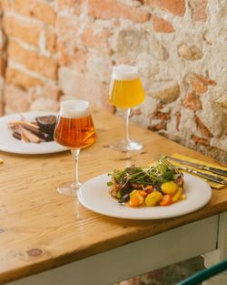 Verres de bière artisanale Baladin avec plats de légumes et viande sur une table en bois contre un mur en pierre.