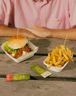 Hamburger und Pommes frites auf einem Holztisch serviert, mit zwei kleinen Soßentütchen seitlich platziert.