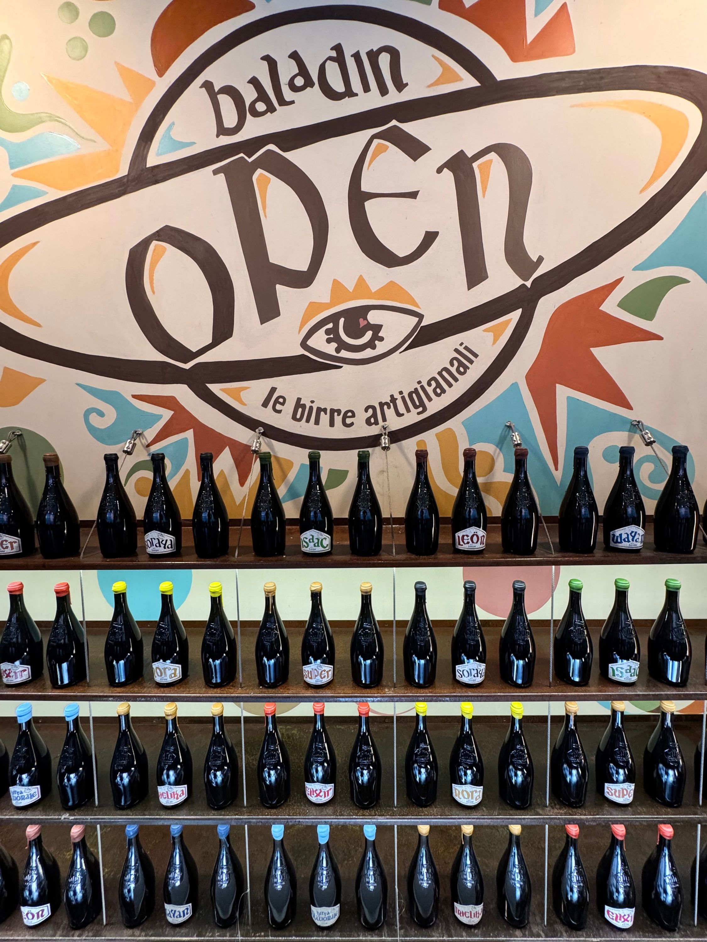 Étagères remplies de nombreuses bouteilles de bière artisanale sous un grand logo mural Open Baladin à Turin.