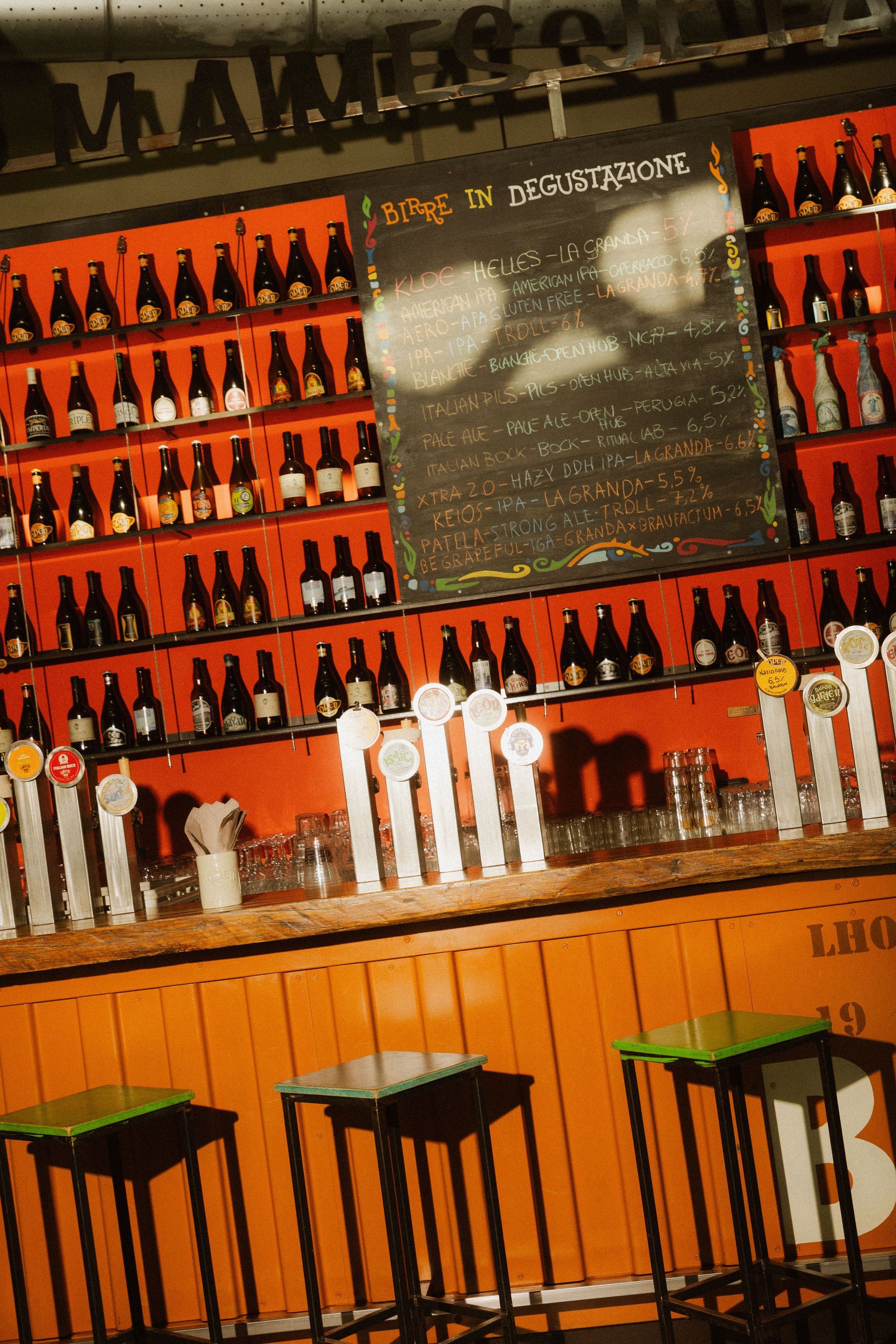 Bar avec une large sélection de bières artisanales sur des étagères rouges chez Open Baladin Cuneo