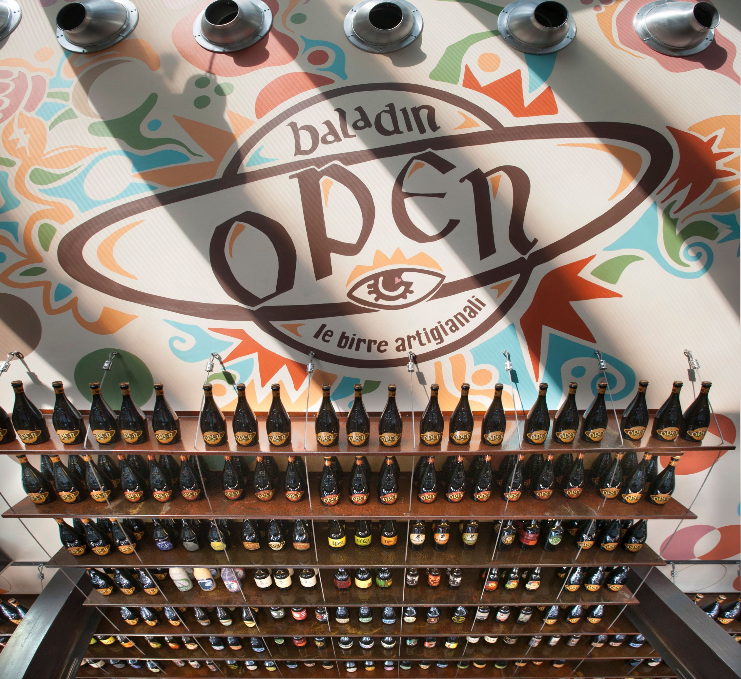 Birre artigianali in esposizione con il logo di Open Baladin Torino sullo sfondo colorato.