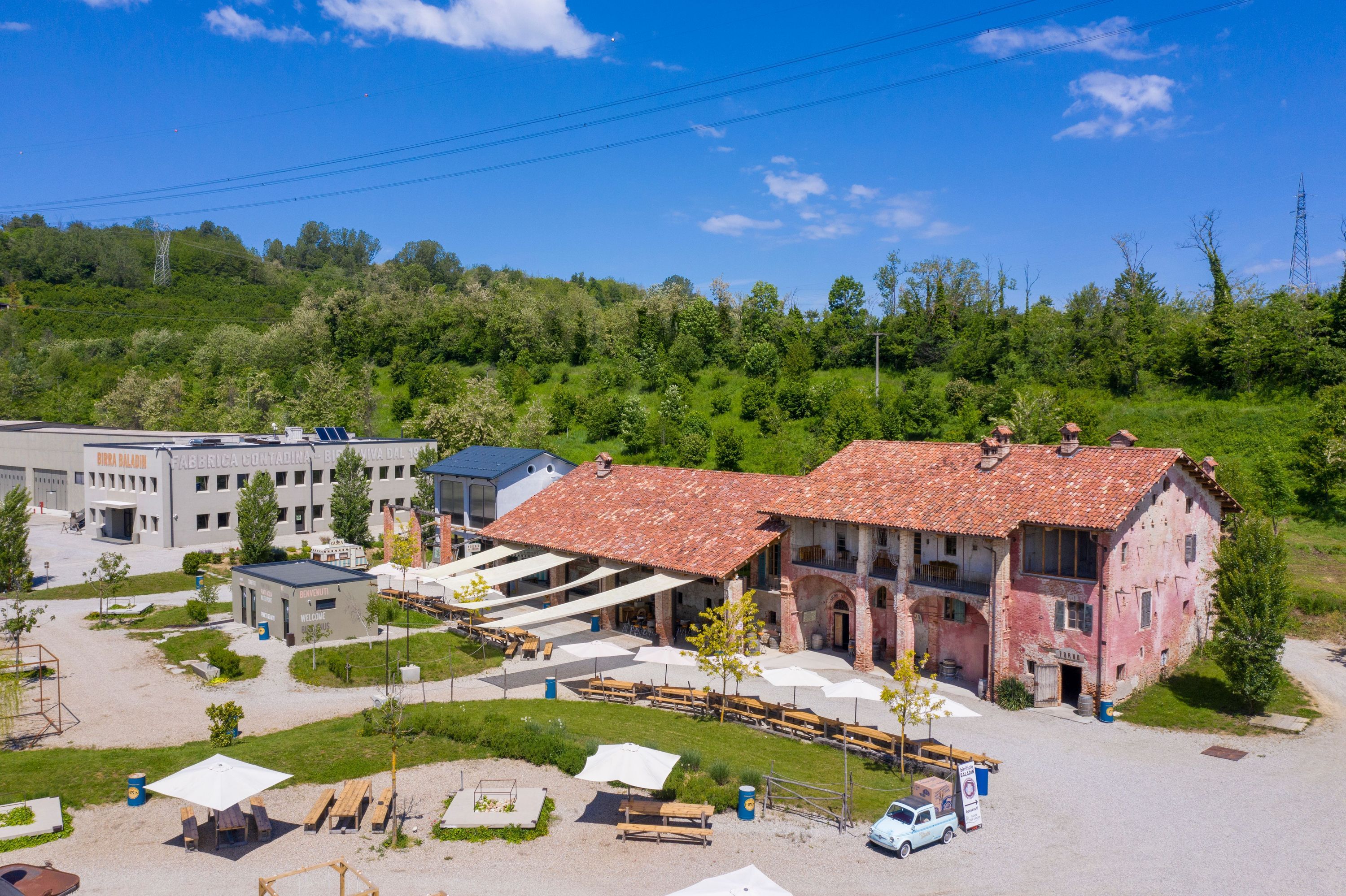Baladin Open Garden outdoor seating area with traditional red-roof building and greenery surrounding the space under blue sky