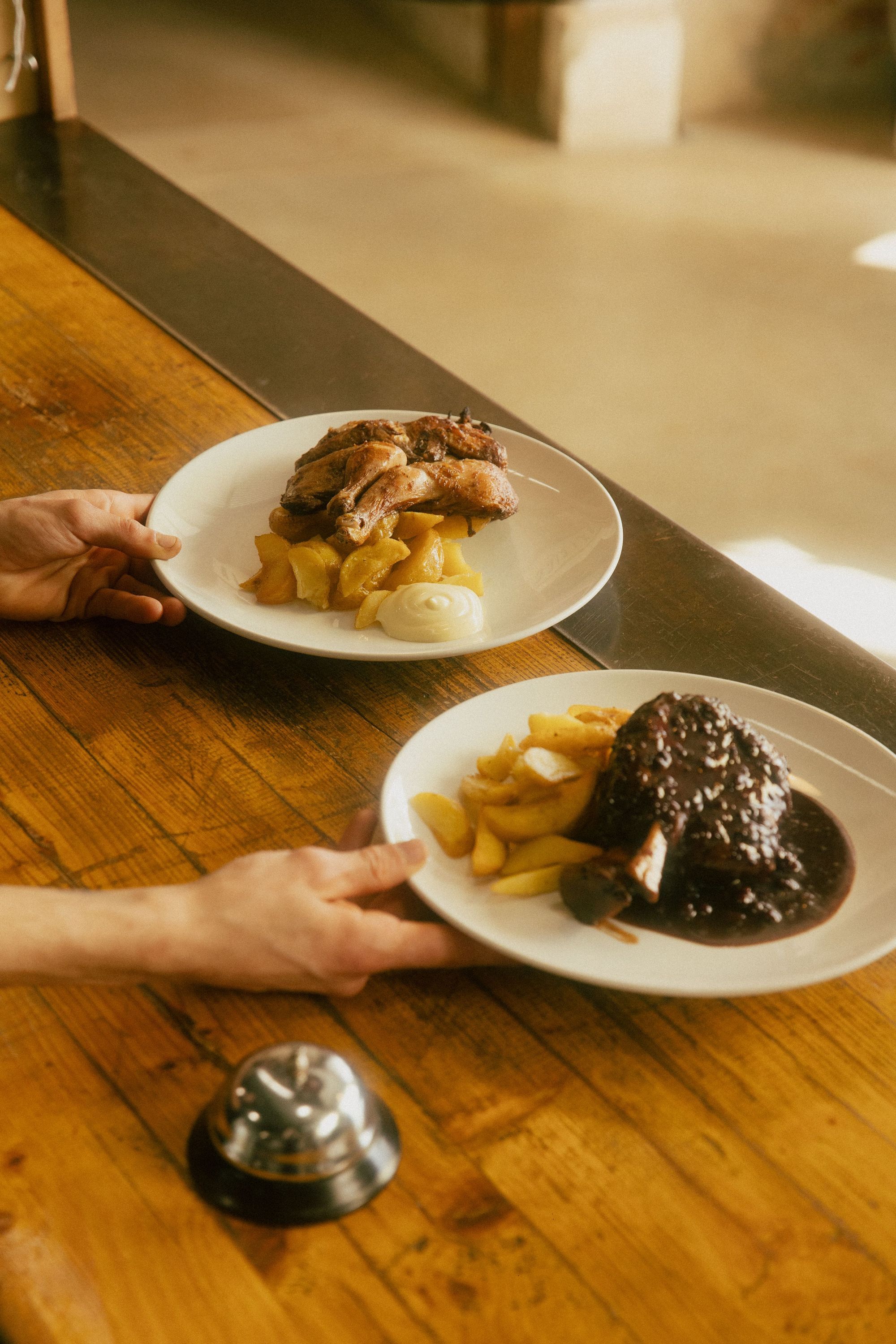 Two plates with dishes including meat and fries on a wooden table at Baladin Open Garden.