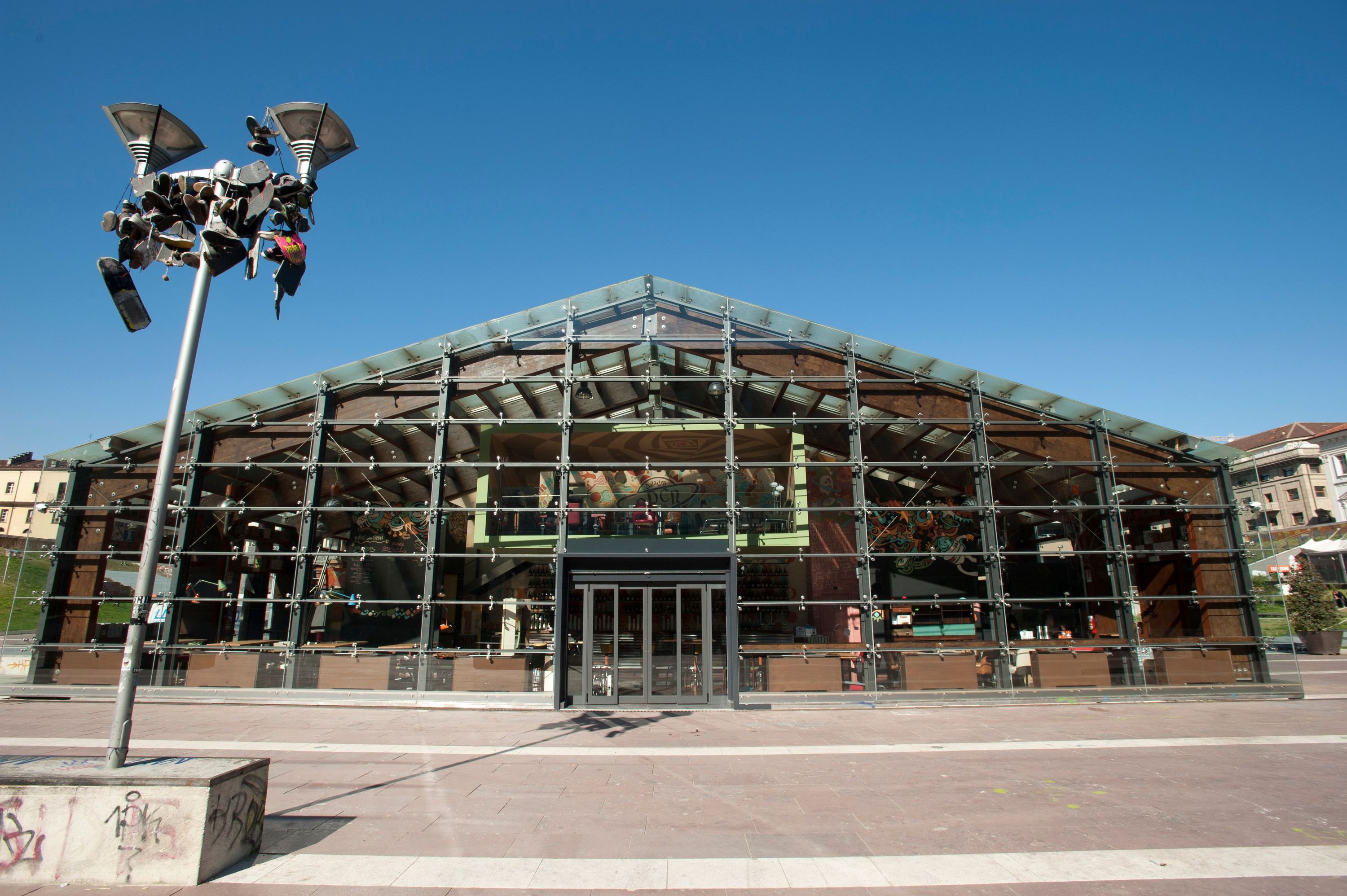 Open Baladin Torino features a large glass facade with metal supports under clear blue sky in an urban setting.
