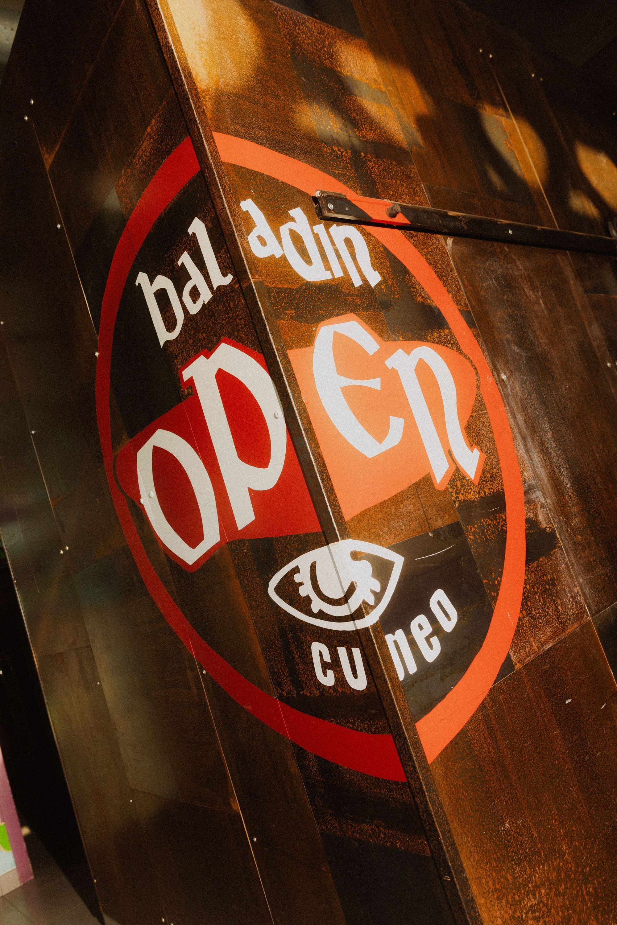 Open Baladin Cuneo logo painted on a rustic wooden door with a circular red and white design.