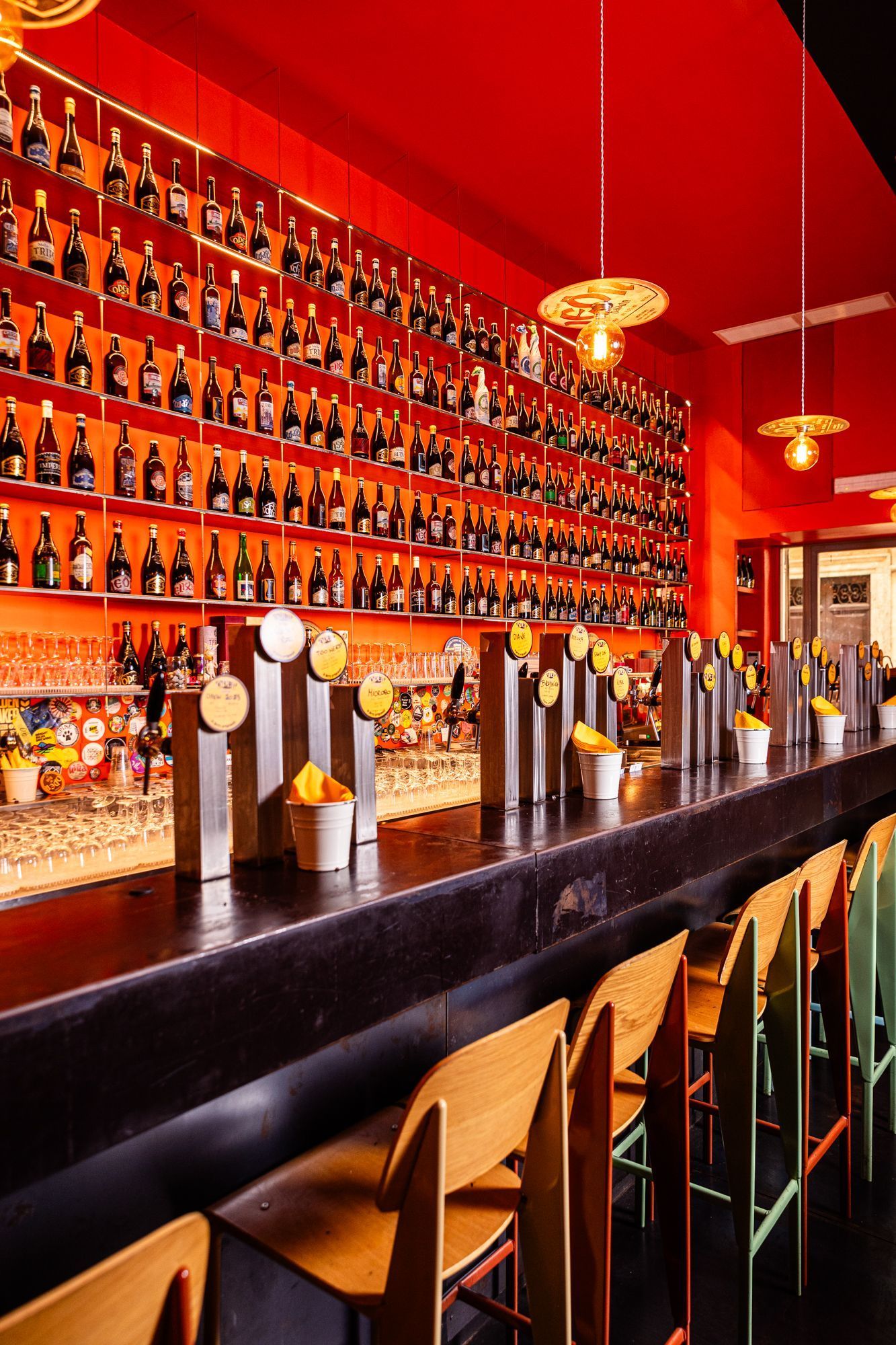 Bar d'Open Baladin Roma avec une longue rangée de bouteilles de bière artisanale et des tabourets en bois alignés.