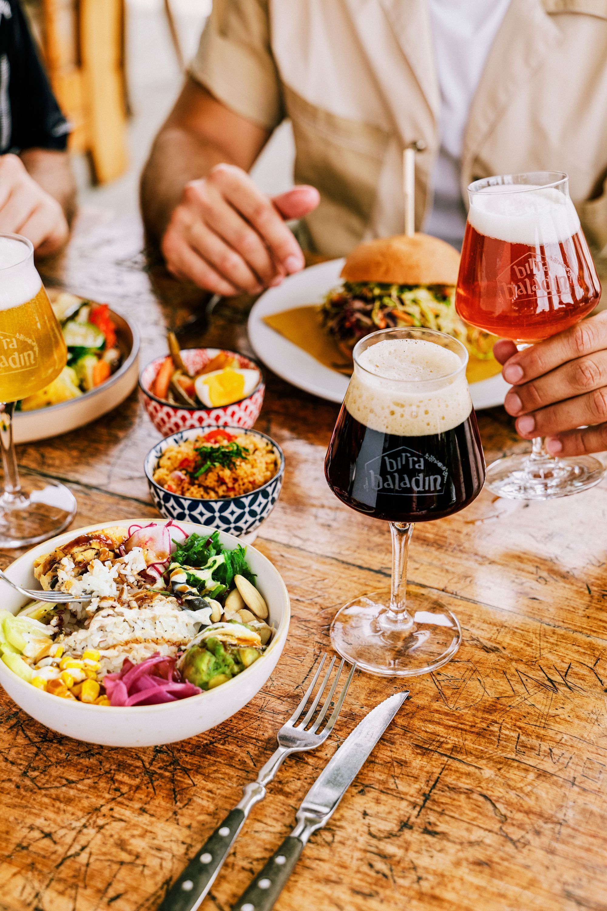 Un tavolo con birra artigianale Baladin, hamburger, insalata e contorni colorati.