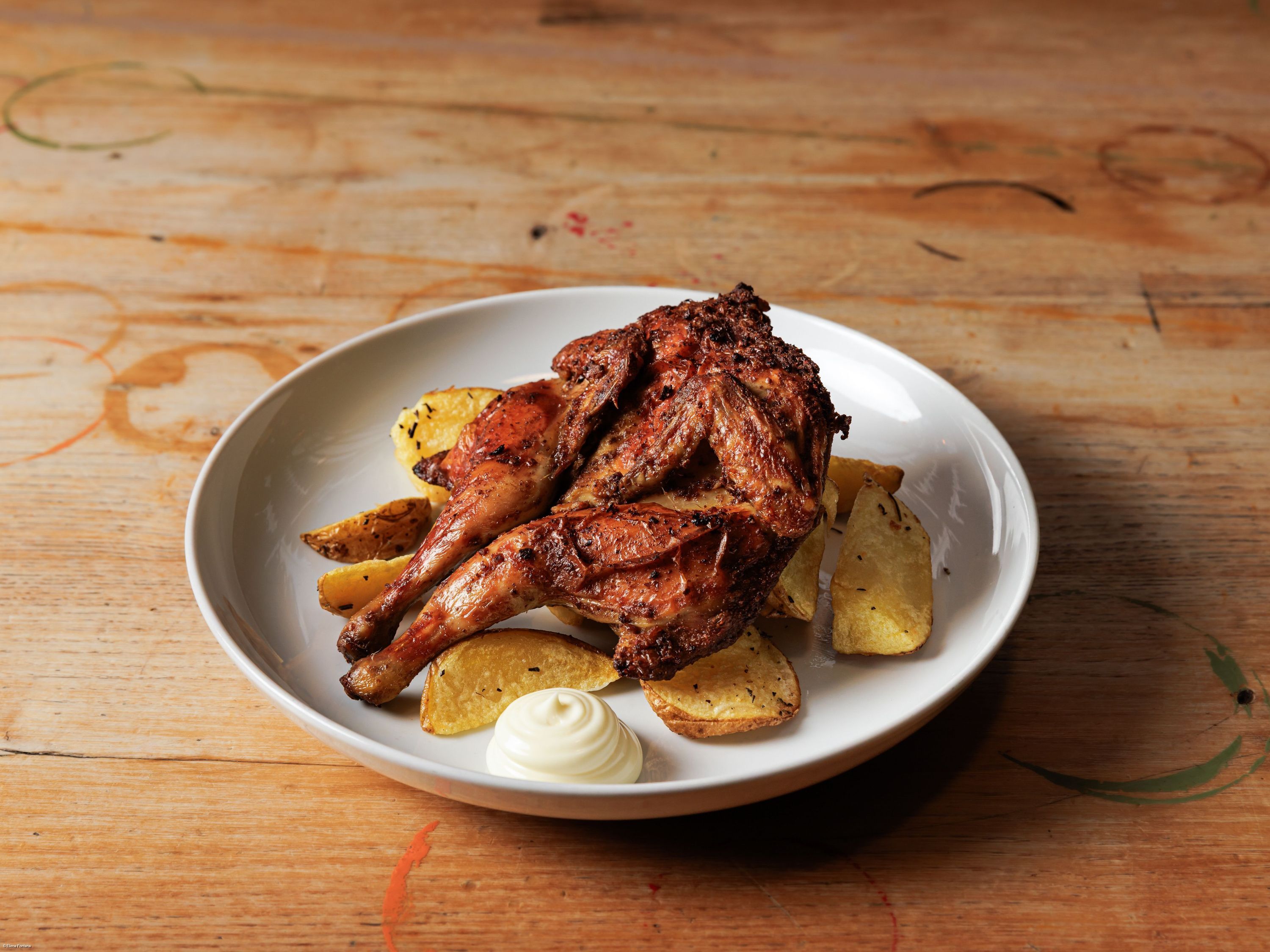 Poulet rôti accompagné de pommes de terre grillées et d'une sauce mayonnaise sur une assiette blanche.