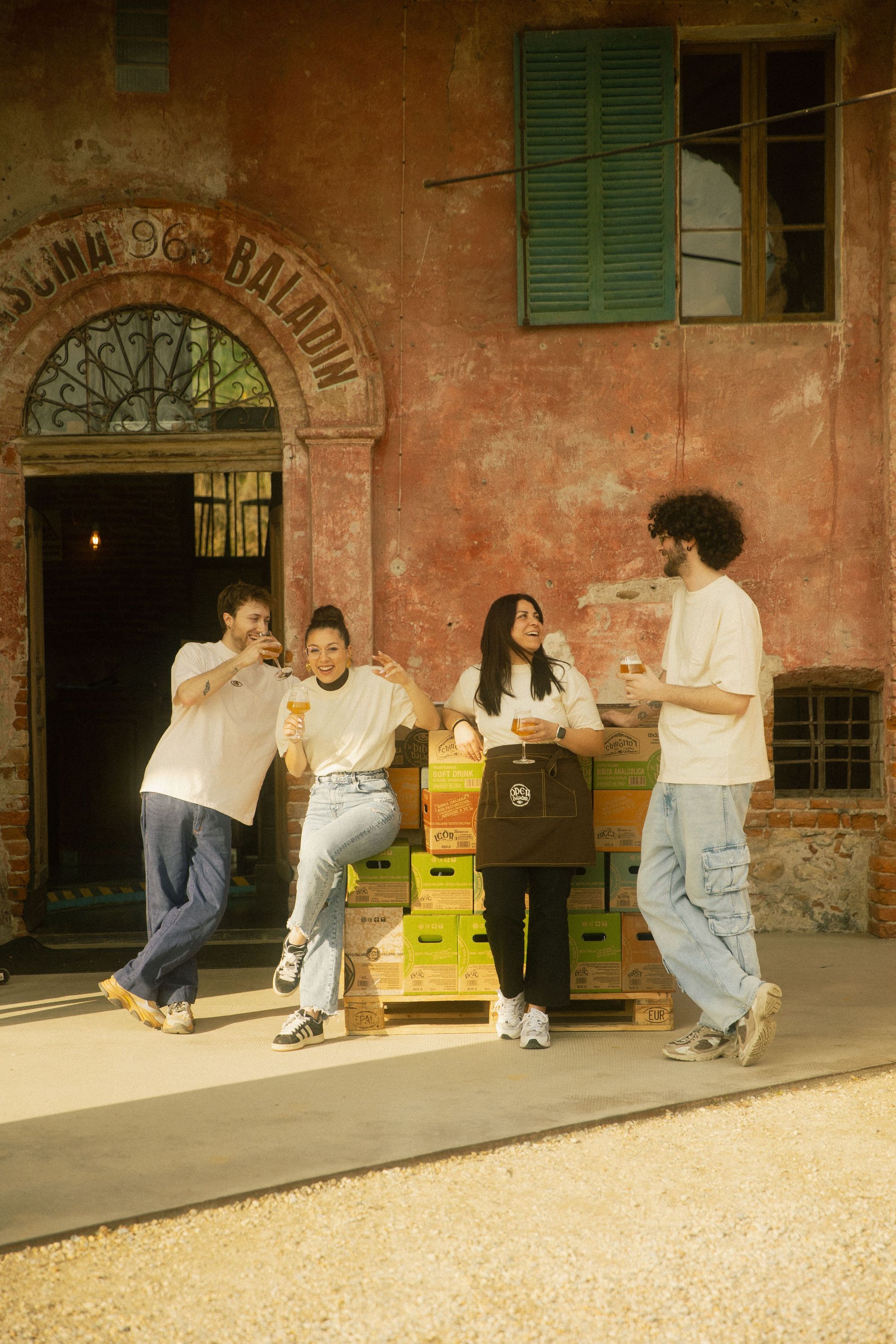 Quattro persone davanti all'ingresso di Baladin Open Garden con cassette gialle e verdi impilate, sorridenti e rilassate.