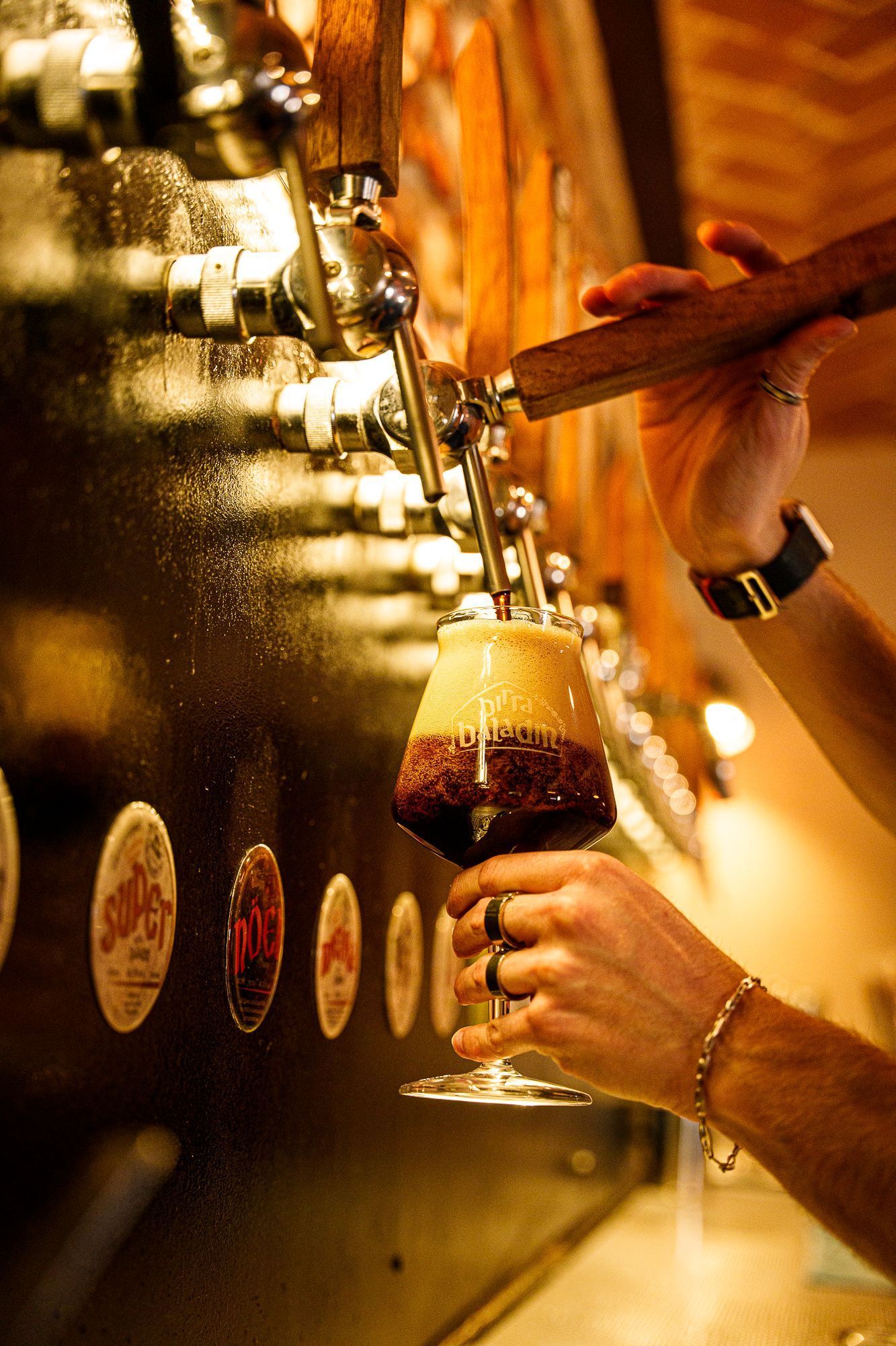 Craft beer being poured from a tap into a Baladin-branded glass in a bar setting.
