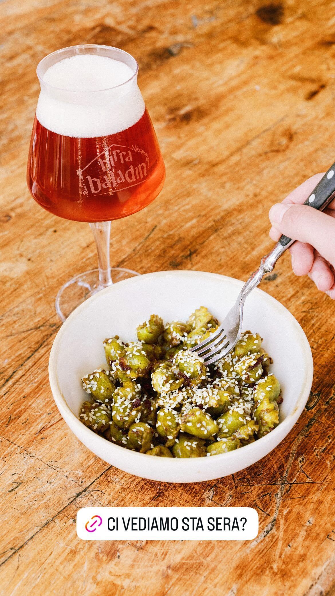 A bowl of dumplings topped with sesame seeds beside a glass of craft beer, highlighting a casual dining experience.