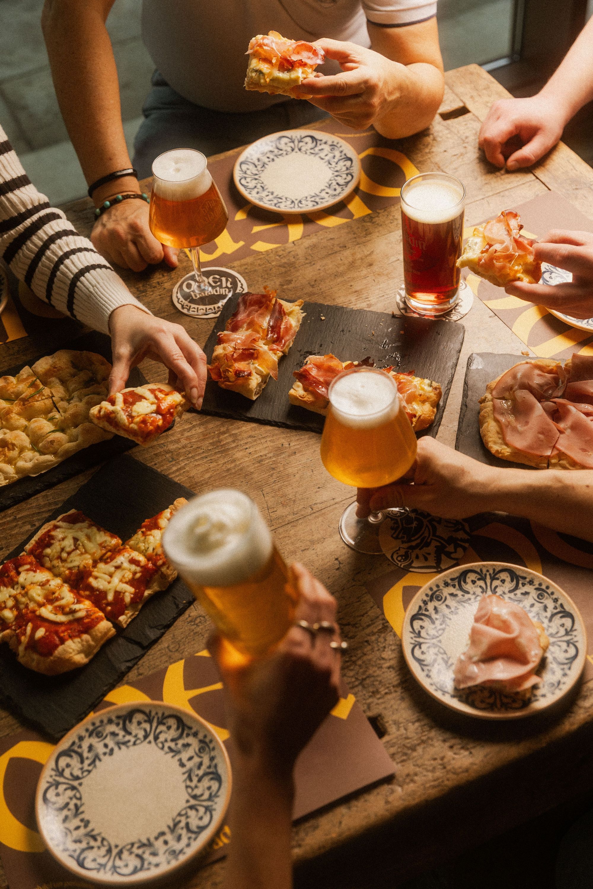 Planches de focaccia et bières artisanales Baladin servies sur une table en bois avec plusieurs convives partageant un repas.