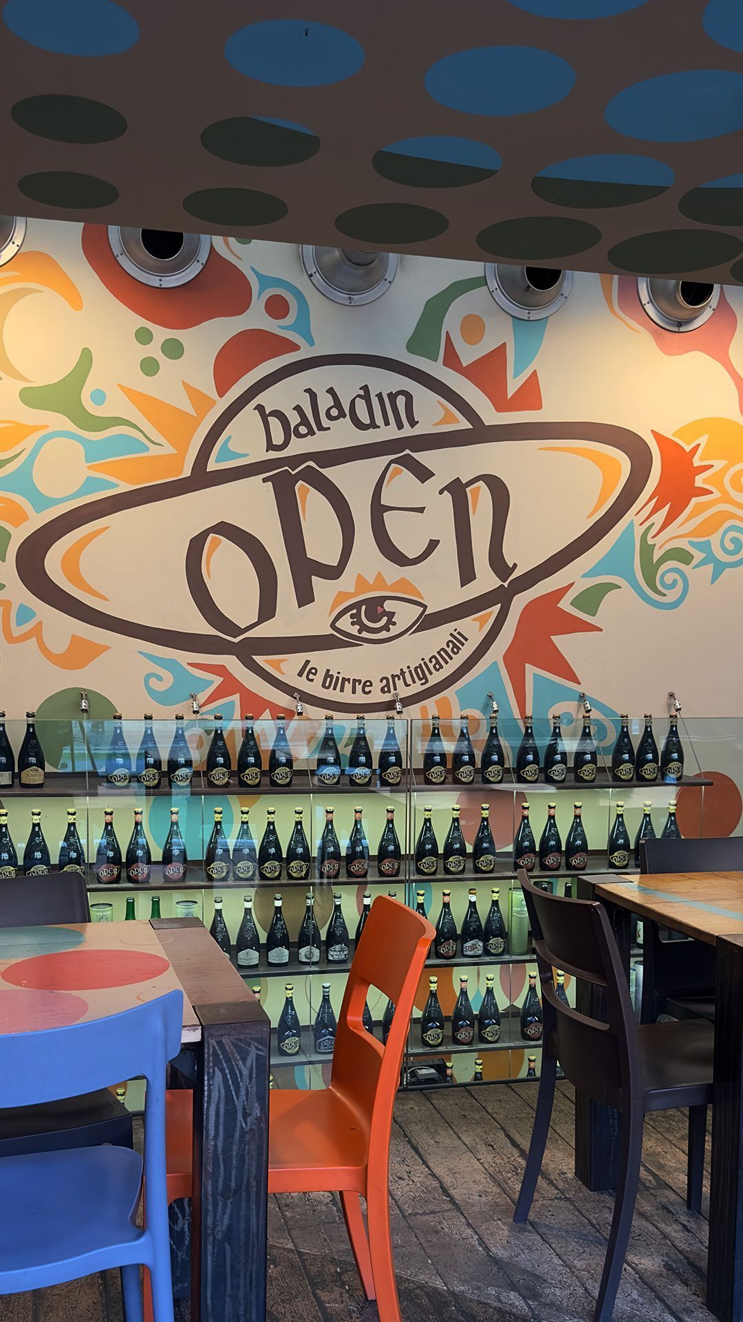Wall mural with Open Baladin logo and craft beer bottles displayed on shelves inside the restaurant.