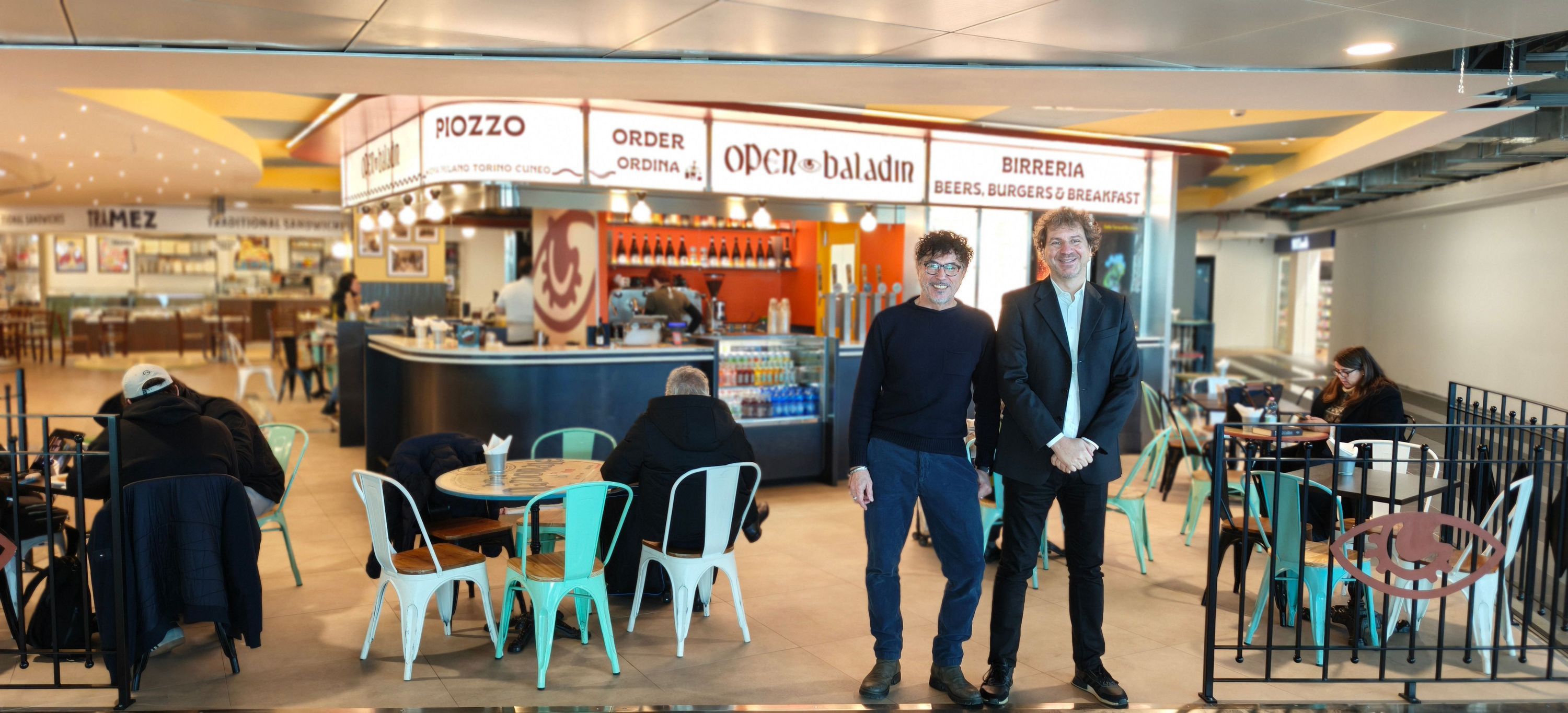 Open Baladin Torino Aeroporto con tavoli, sedie colorate, e bancone per birra artigianale e hamburger.