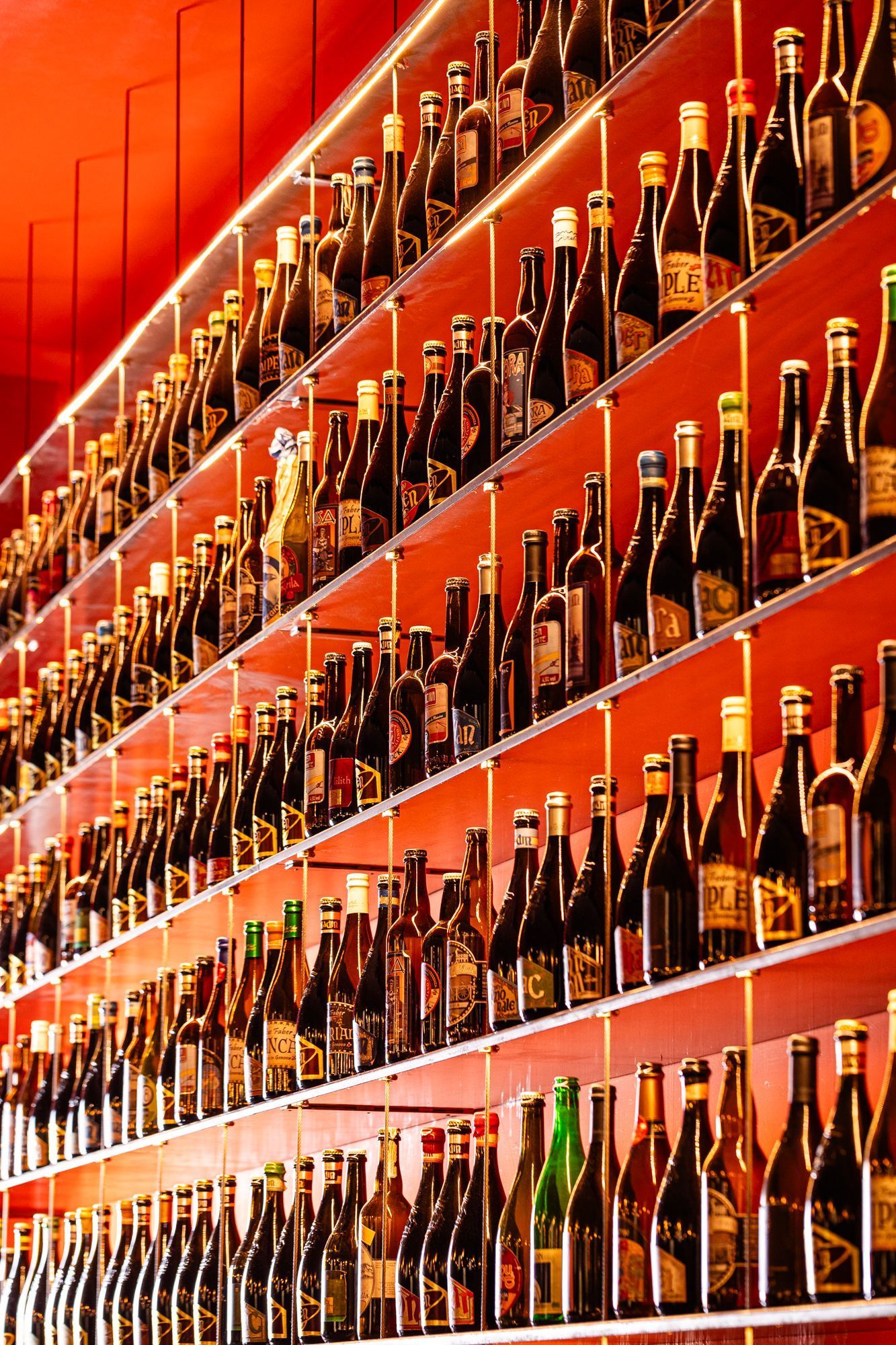 Scaffali con numerose bottiglie di birra artigianale allineate in un locale dal design moderno e colori caldi.