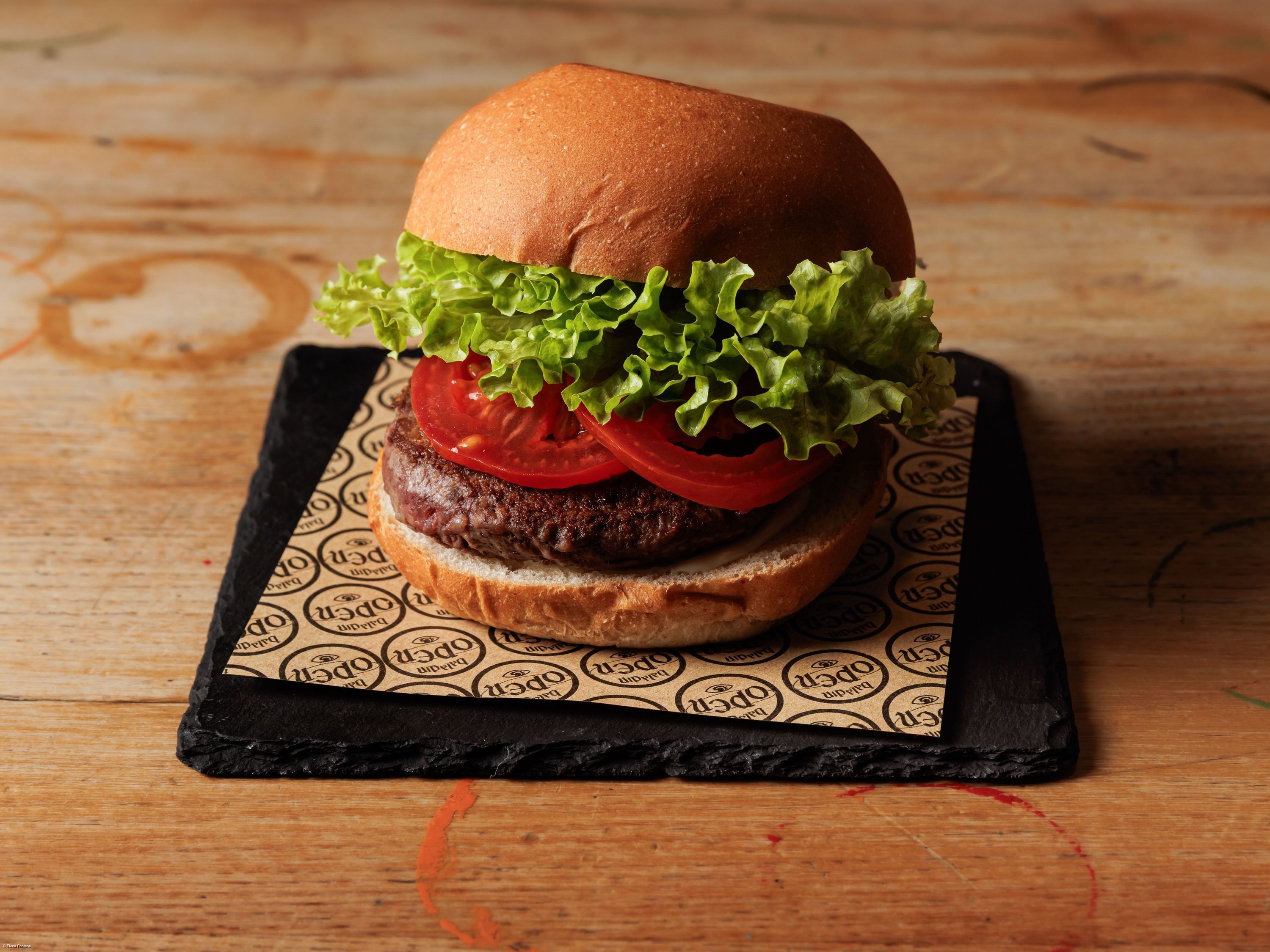 Hamburger avec laitue et tranches de tomate sur un plateau noir, servie chez Open Baladin Torino Aeroporto.