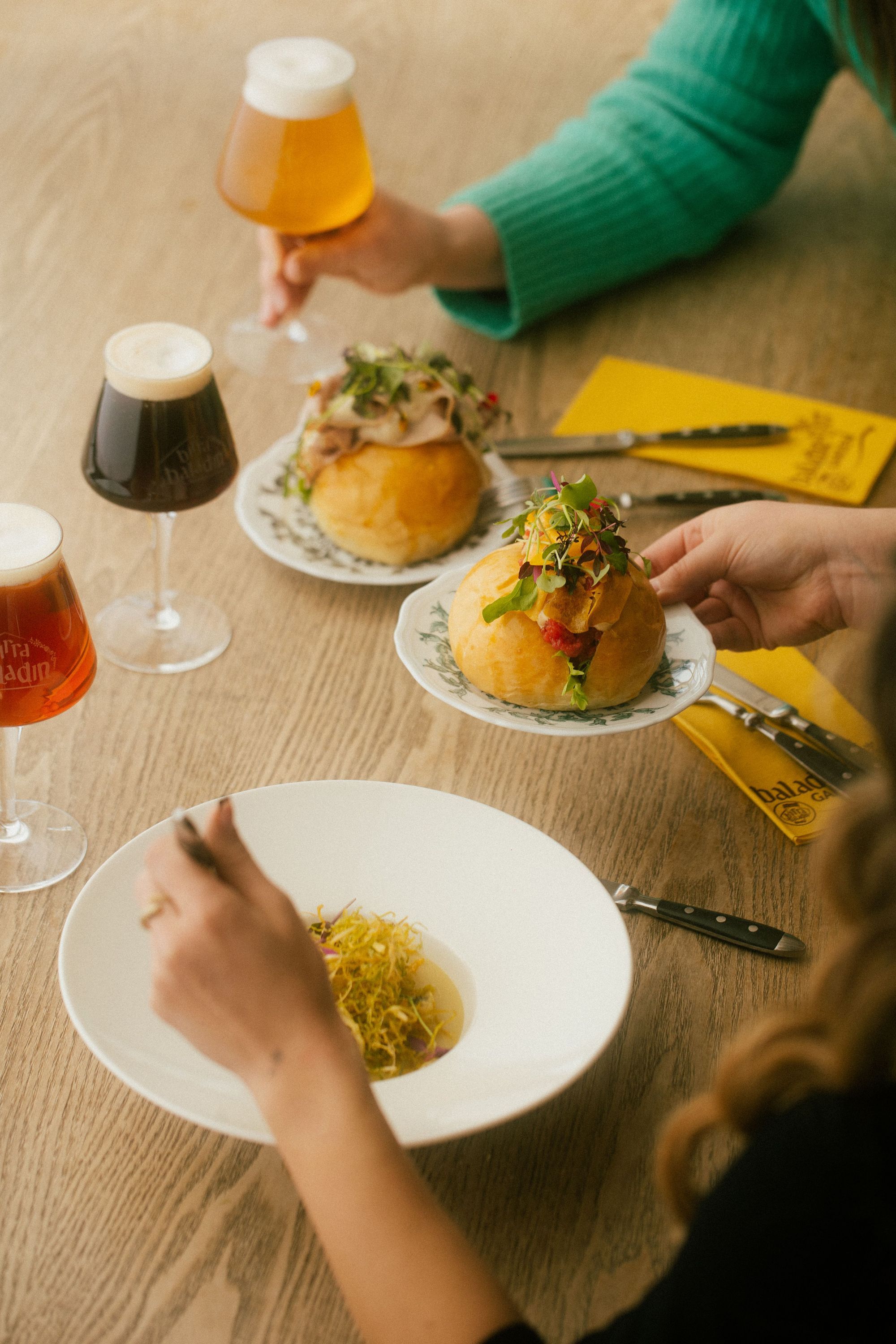 Due hamburger e tre bicchieri di birra artigianale serviti su un tavolo di legno in Baladin Open Garden.