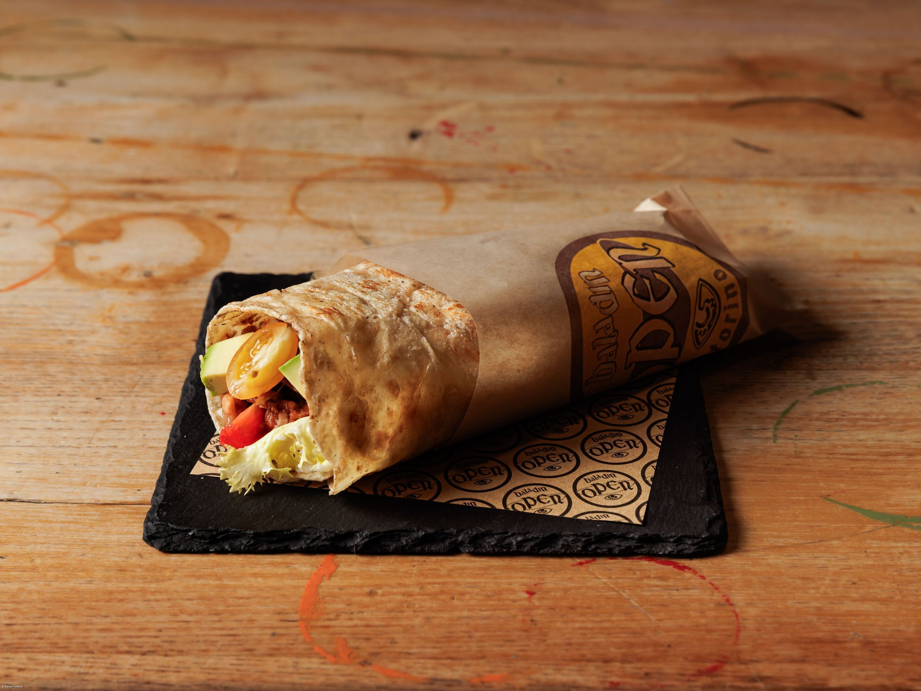 Wrap sandwich with fresh vegetables and meat wrapped in printed paper on a rustic wooden table