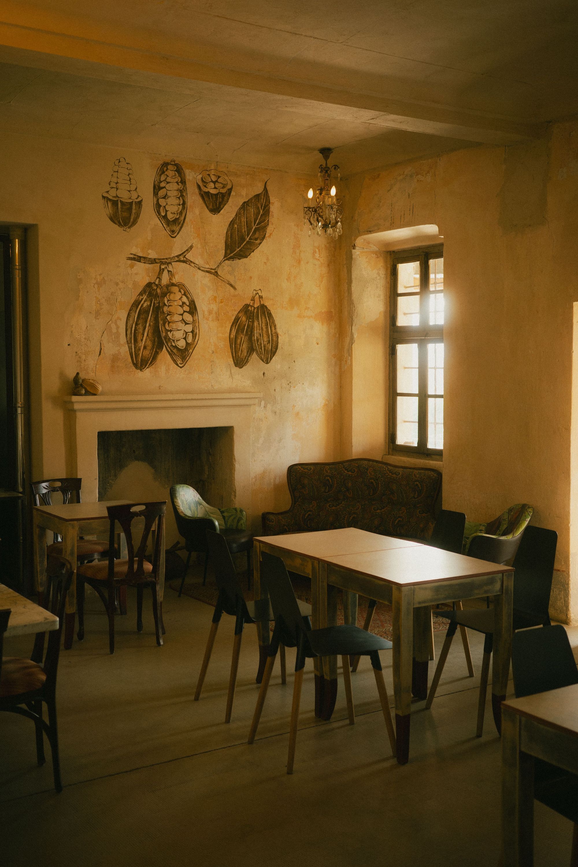 Rustic interior of Baladin Open Garden with wooden tables, chairs, and cocoa bean wall art near a window.