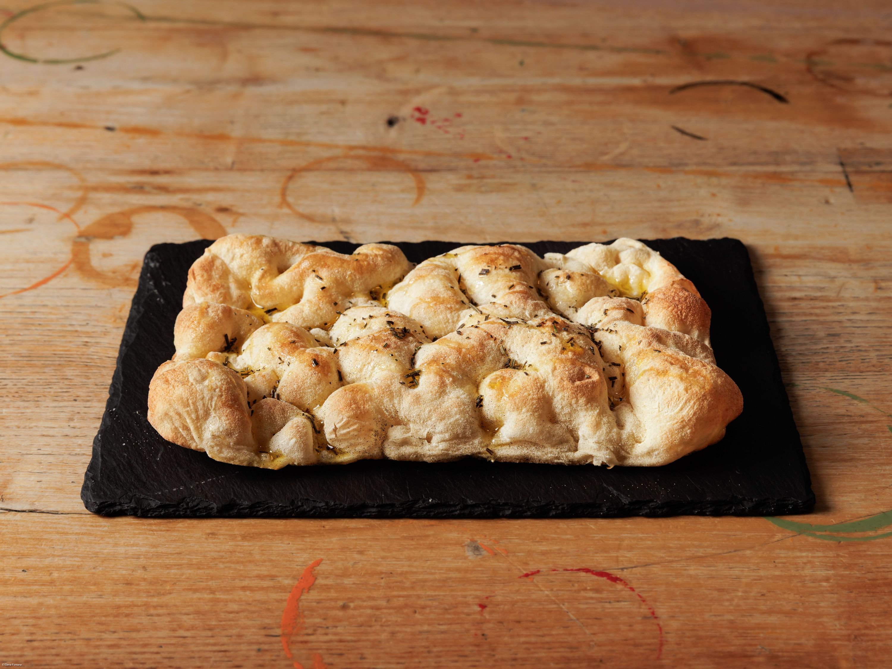 Focaccia italienne traditionnelle posée sur une ardoise noire sur une table en bois rustique.