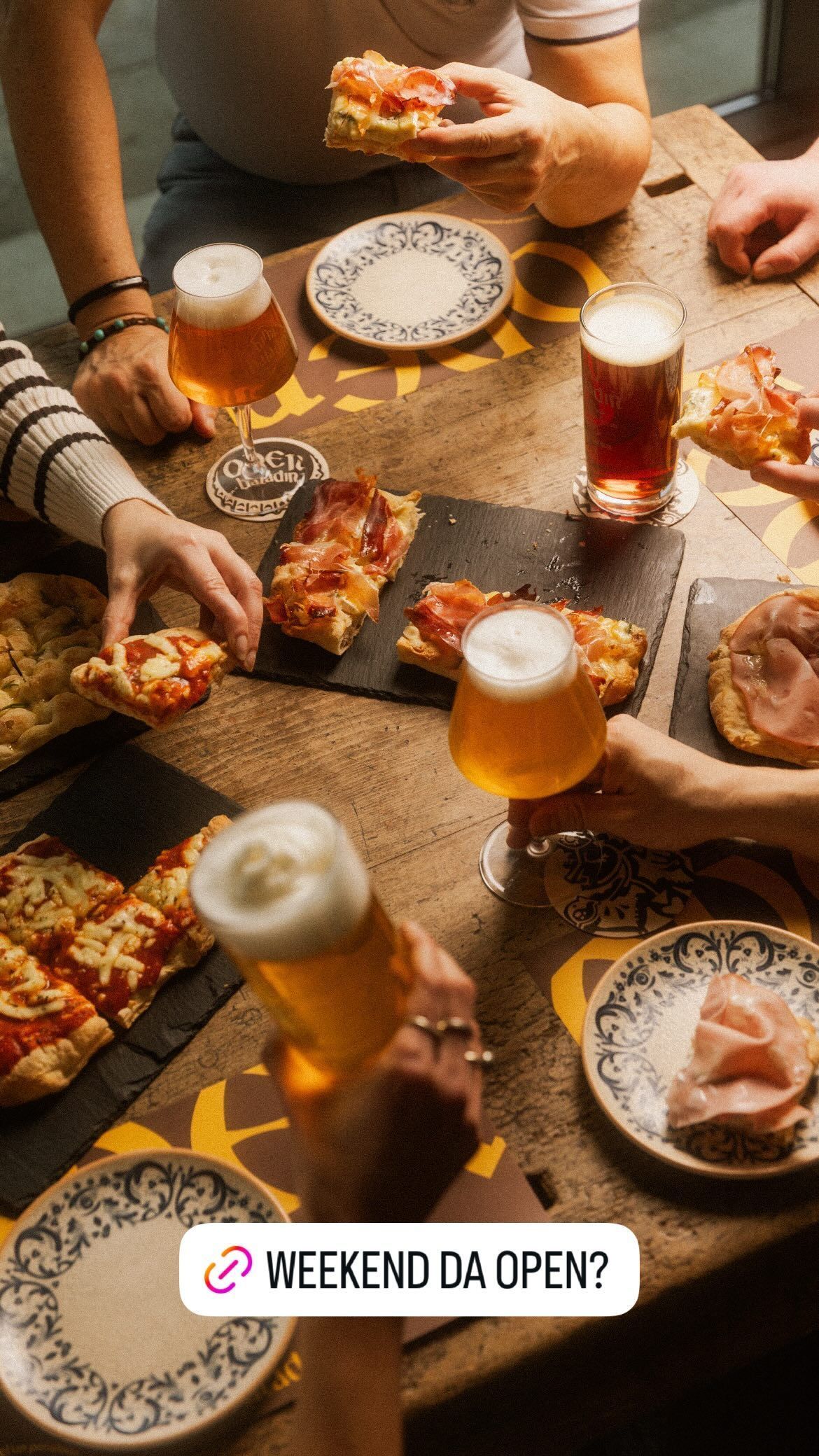 Persone che condividono birra artigianale Baladin e hamburger su tavolo di legno con piatti decorati.