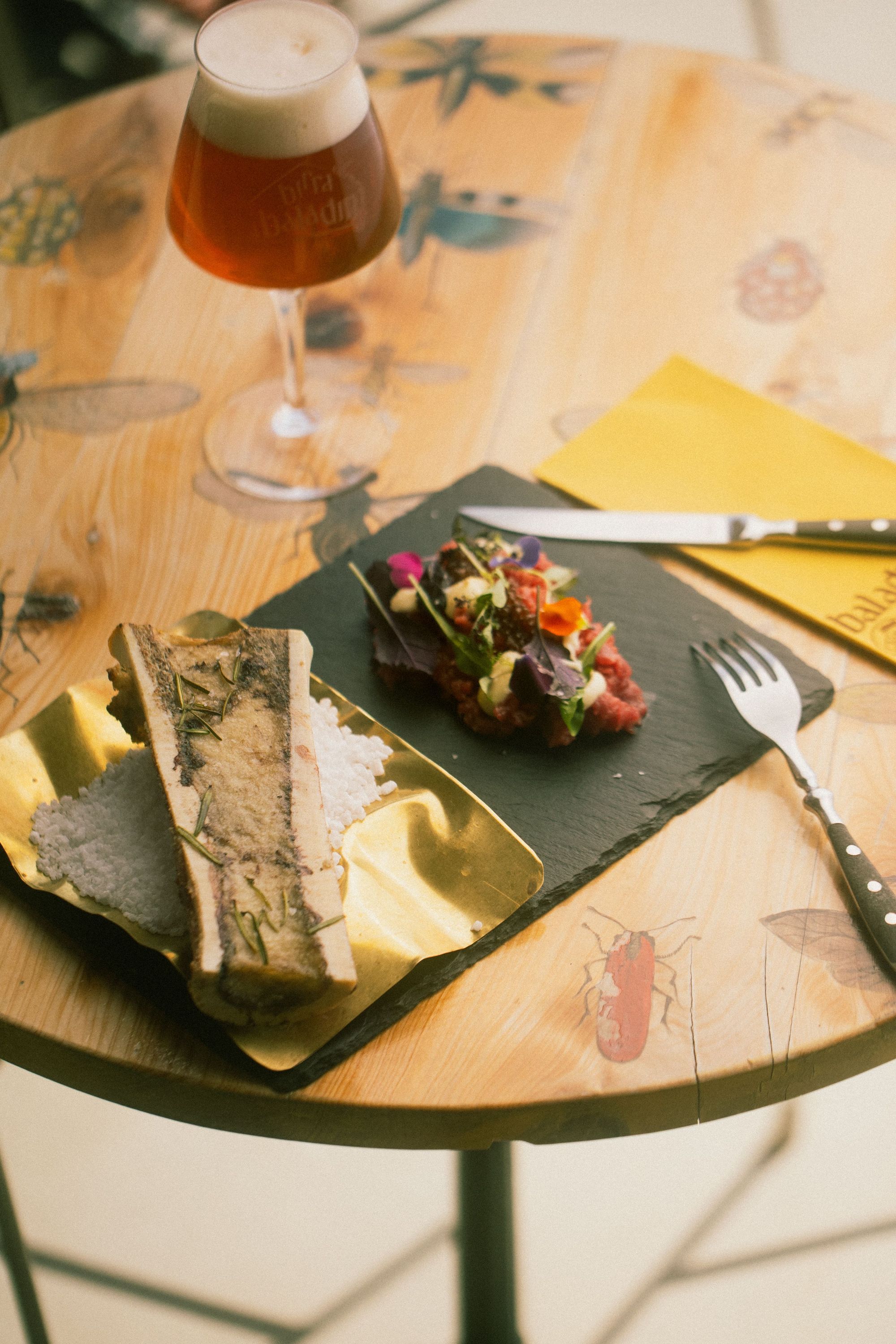 Birra artigianale Baladin servita con hamburger e pane su tavolo in legno rustico con posate.