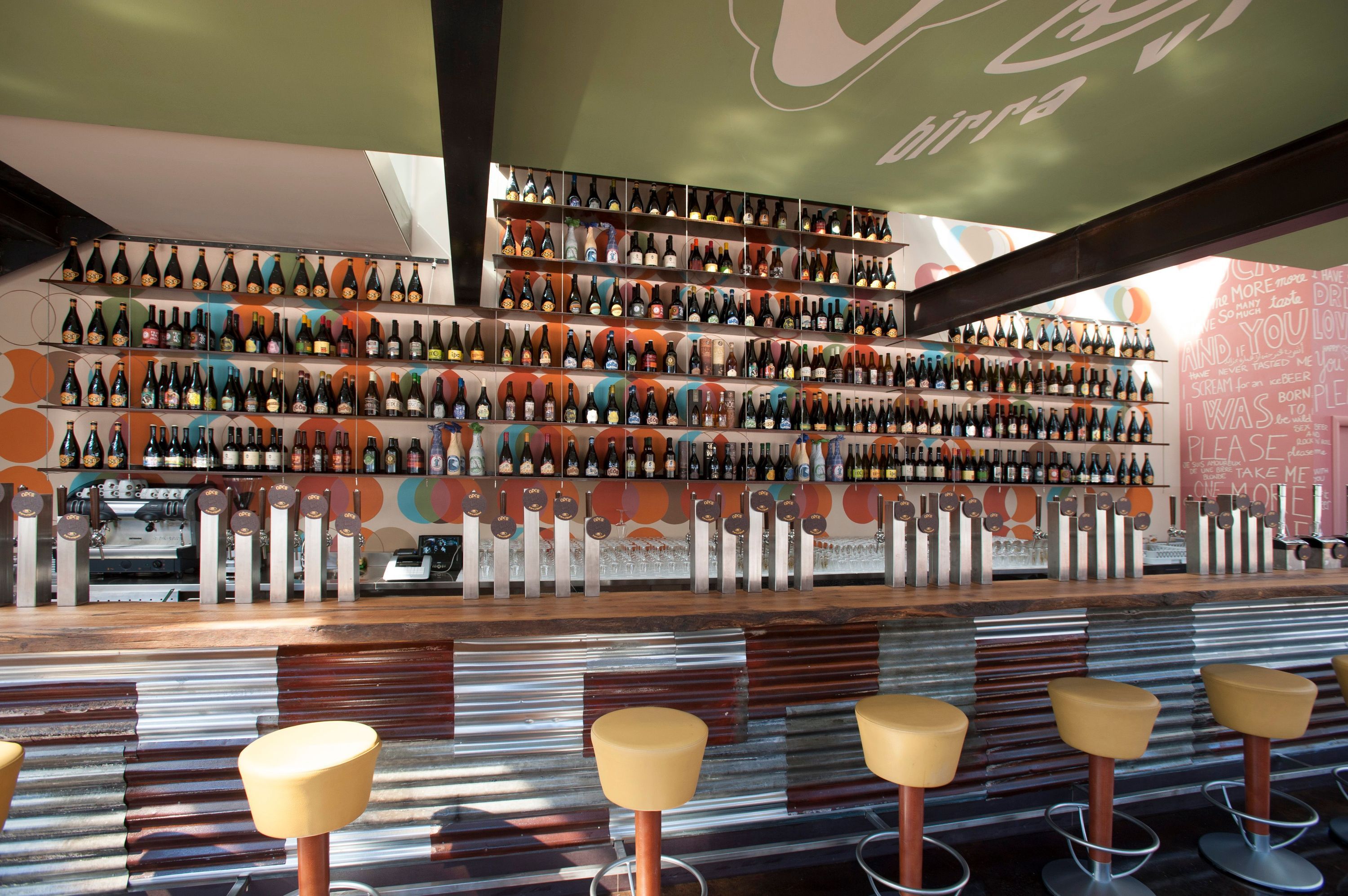 Bar area at Open Baladin Torino with rows of craft beer bottles on shelves and multiple beer taps on the counter.