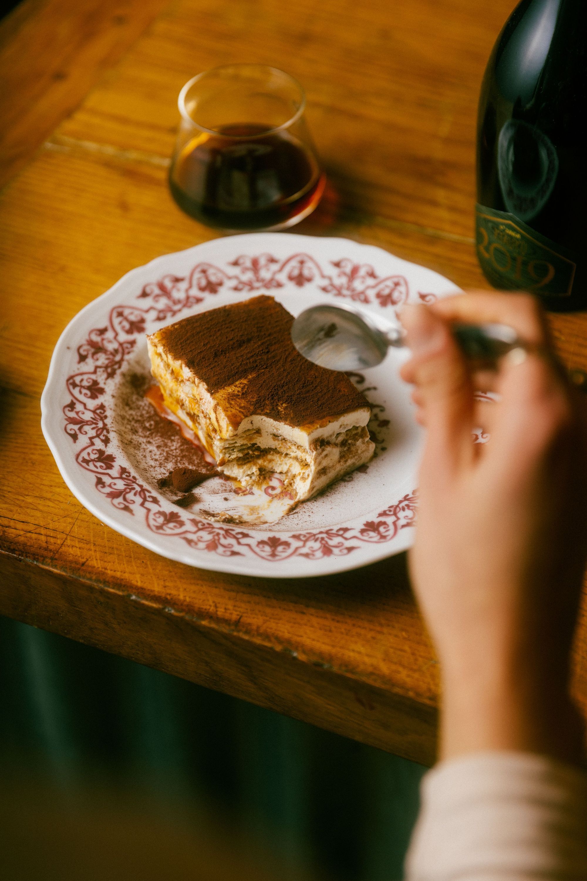 Tiramisu dessert on a decorative plate with a glass of craft beer and bottle on a wooden table at Baladin Open Garden.